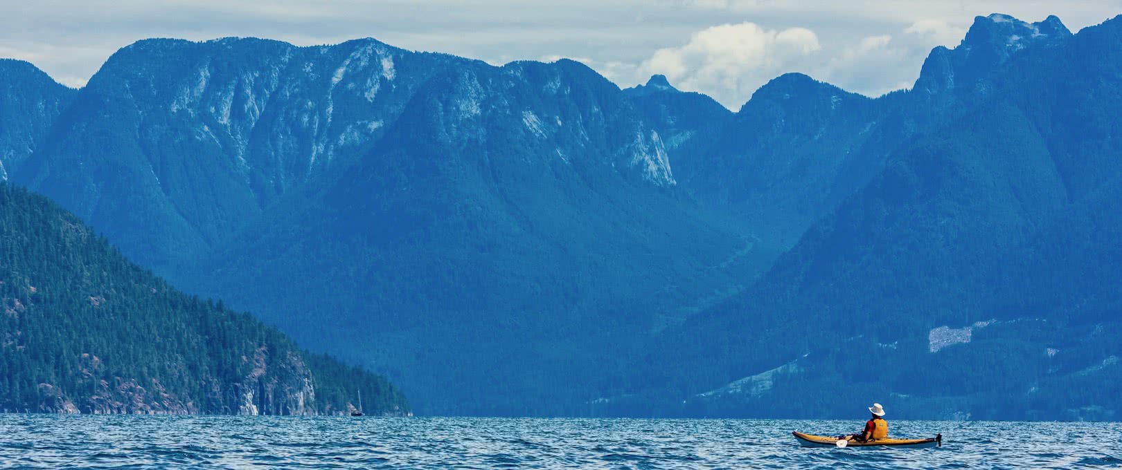 A kayaker sits and looks at the Coast Mountains on one of our multi-day kayak tours