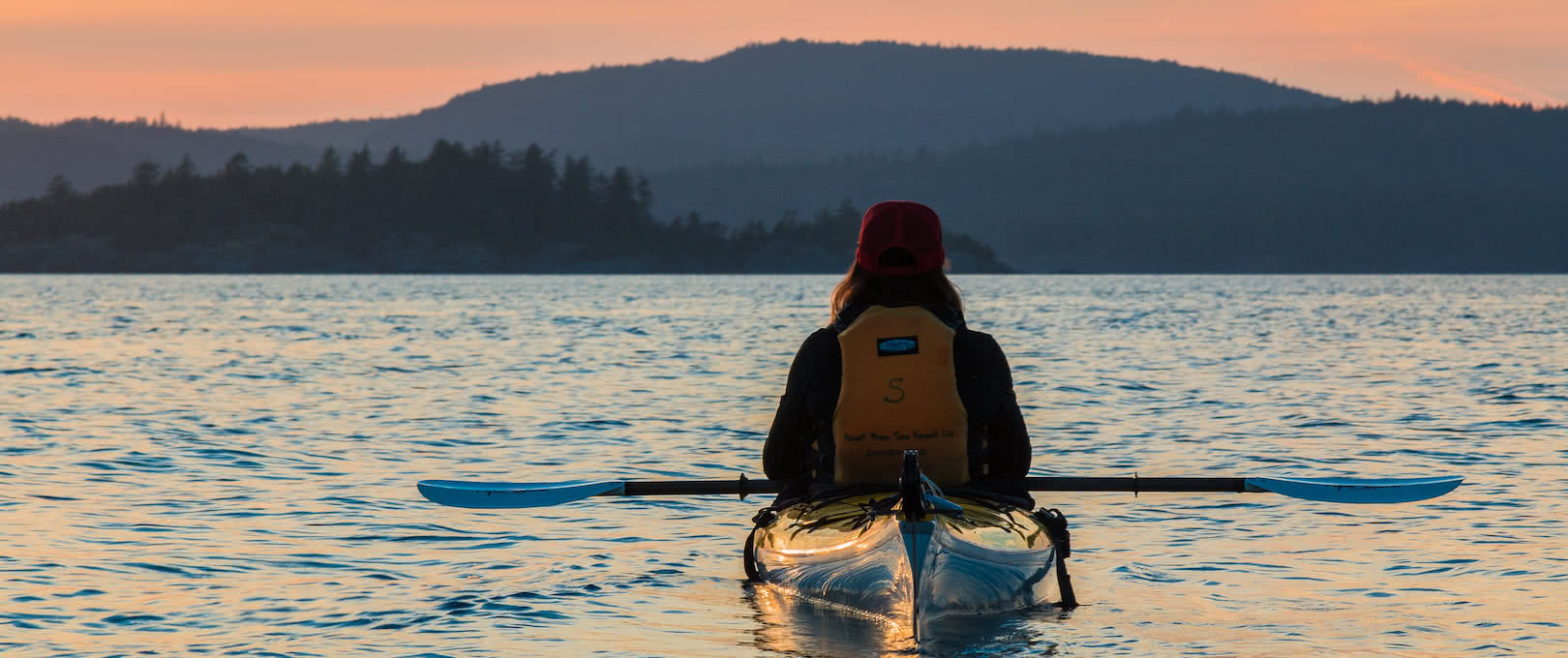 A guest watches the sunset from her kayak on a multi-day camping tour