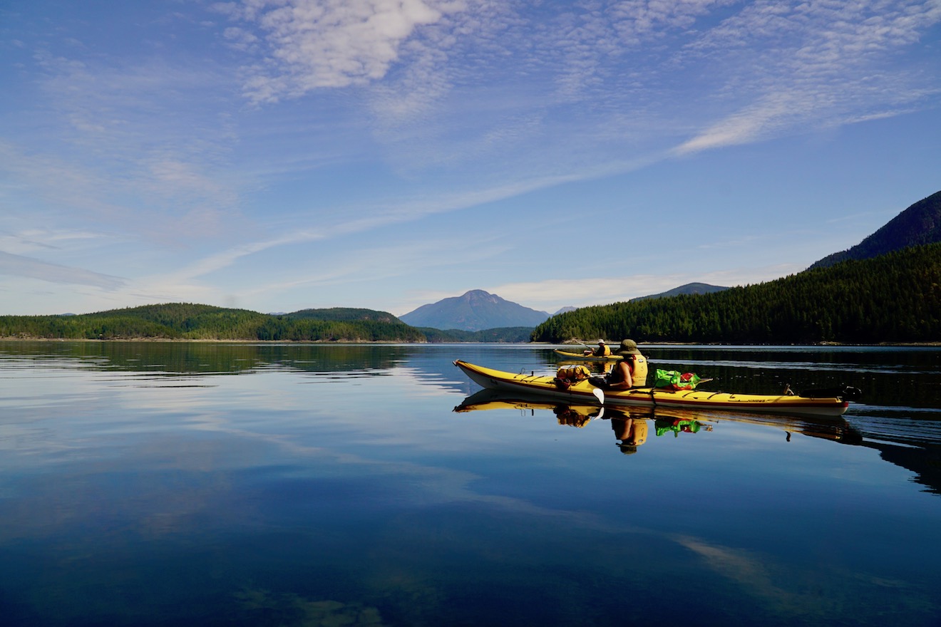 Two kayakers paddling on glassy calm water in Okeover Inlet in Desolation Sound