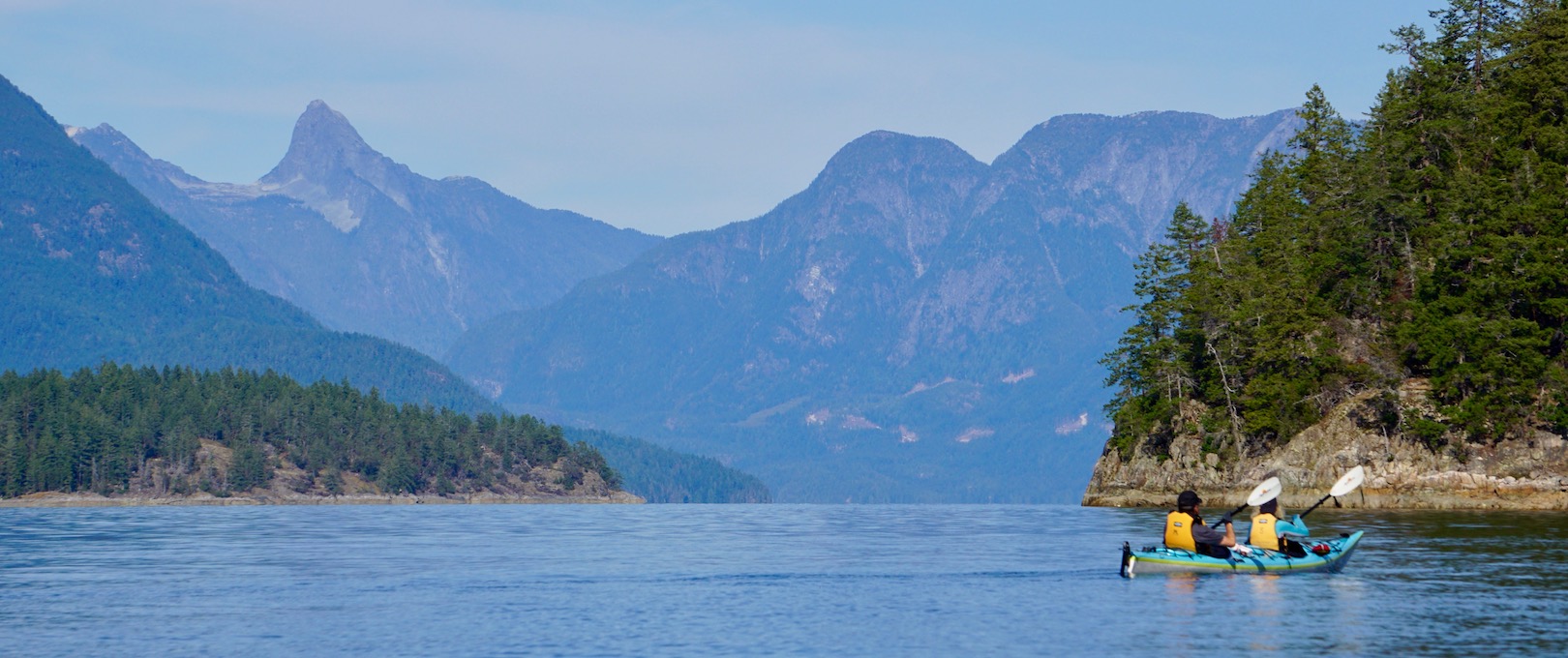 Paddlers in a double kayak paddle in Desolation Sound with Mount Denman in the background