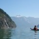 A kayaker paddles towards a large waterfall on a sunny day in Toba Inlet