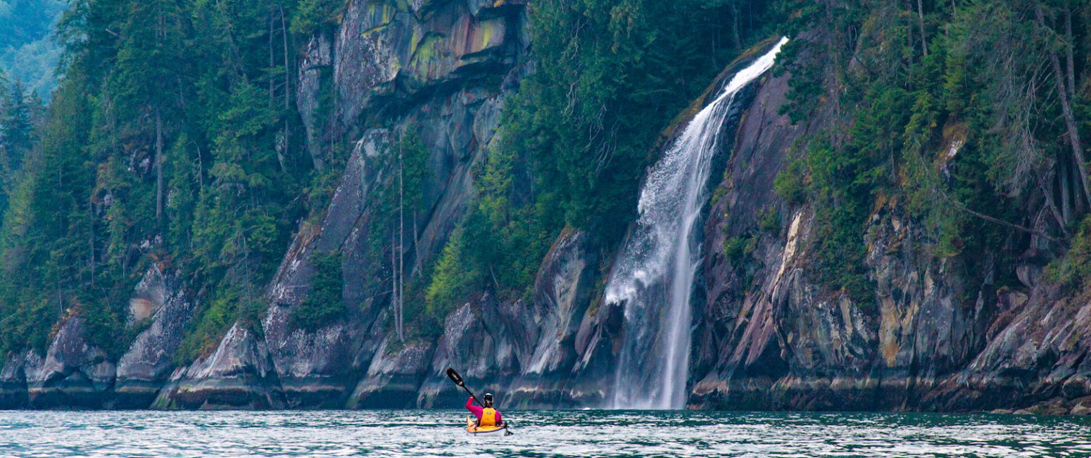 A kayaker approaches a waterfall in Toba Inlet on a sea kayak expedition