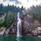 A kayaker poses with paddle in the air beneath an epic waterfall in Toba Inlet